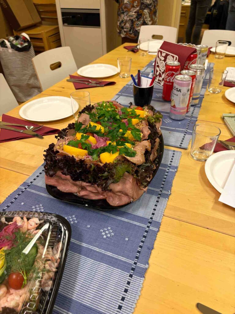 Smörgåstårta, räkmacka och drickor uppdukade på bordet med tallrikar och bestick.