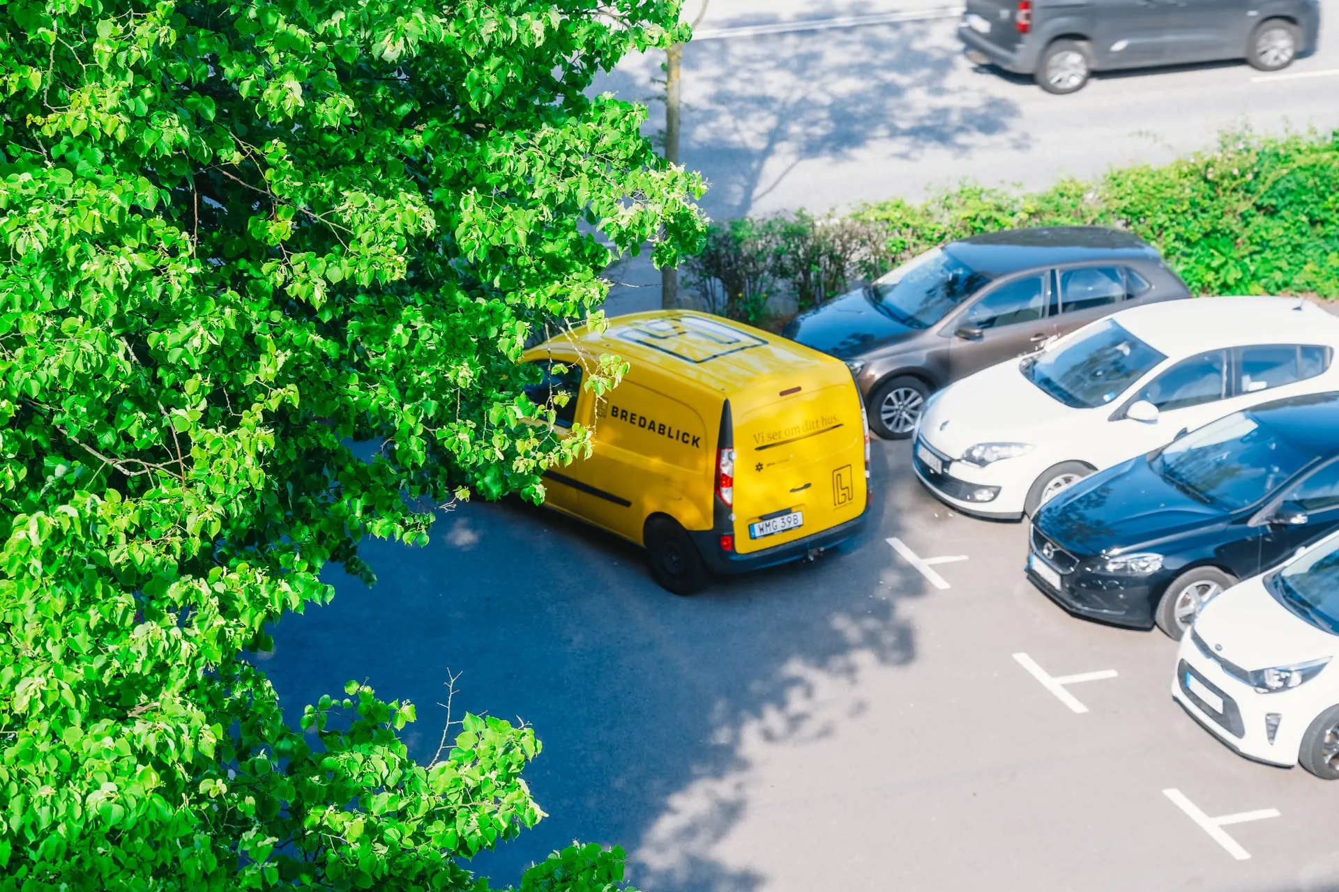 Gul servicebil från Bredablick parkerad vid bostadsfastighet, omgiven av grönskande träd.