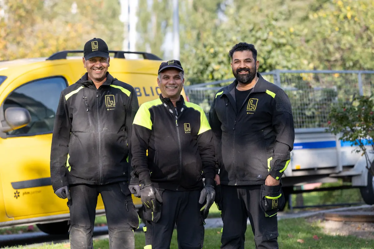Tre fastighetsskötare från Bredablick i arbetskläder framför en gul servicebil vid en fastighet i Stockholm.